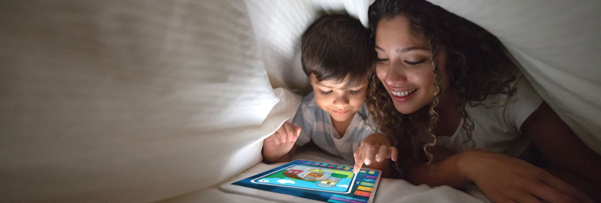 Woman and her son in a blanket fort playing on an iPad.